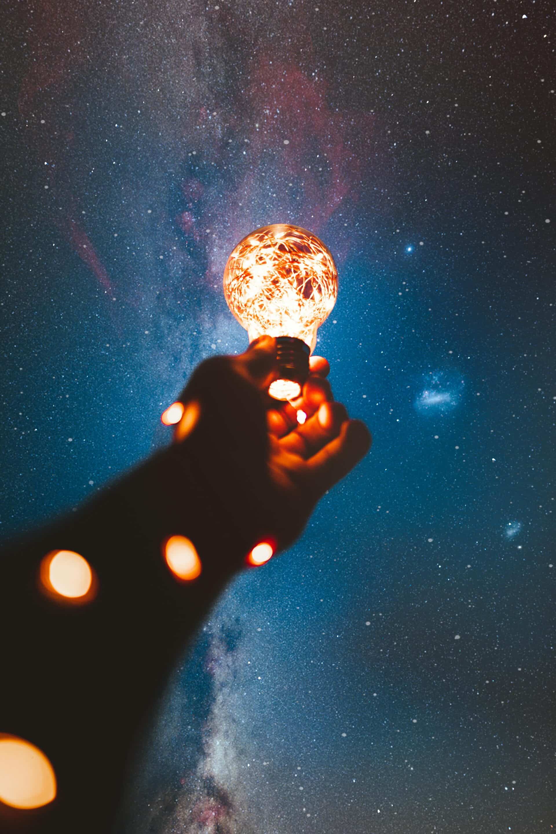 Hand holding a glowing light bulb against a starry sky representing Cotes Code generating AI driven search visibility for businesses in Grand Rapids, Ada, and surrounding West Michigan